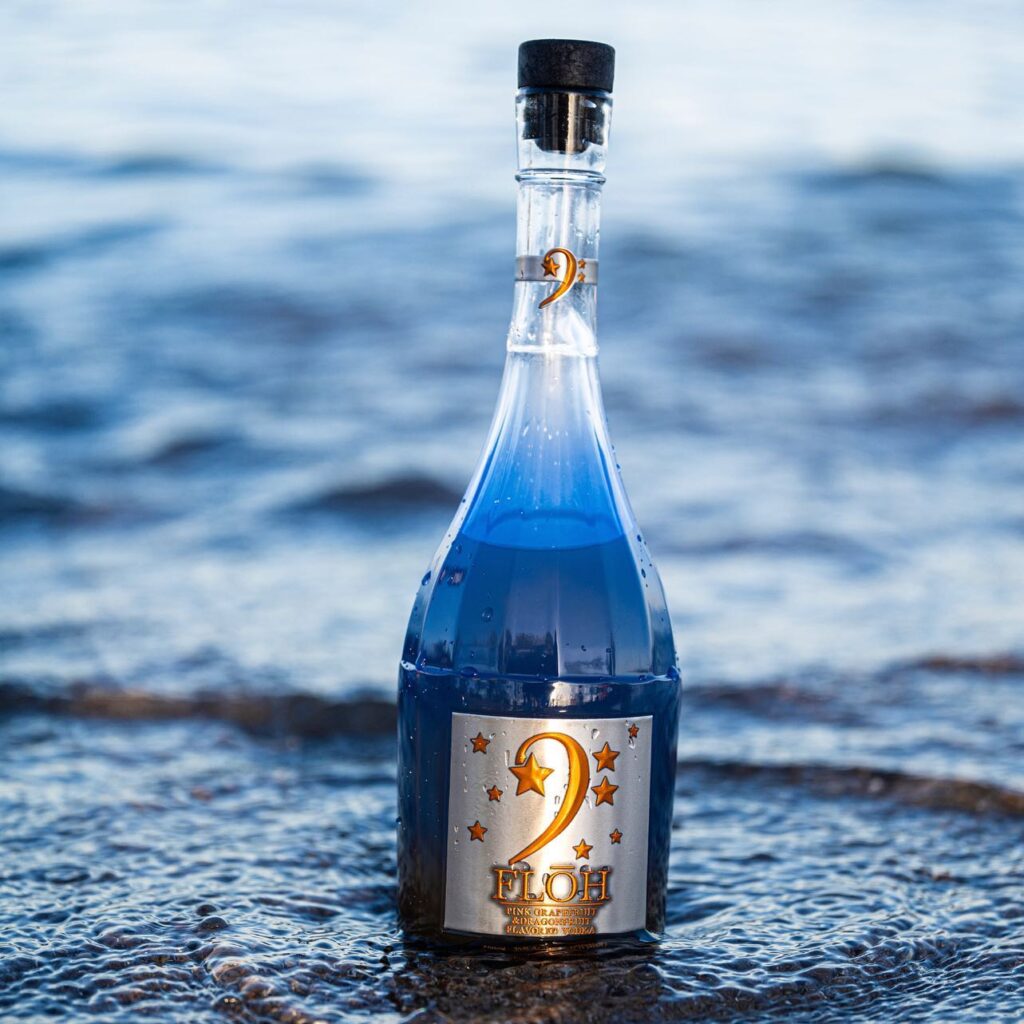 a bottle of black owned Floh Vodka on a beach with water receding