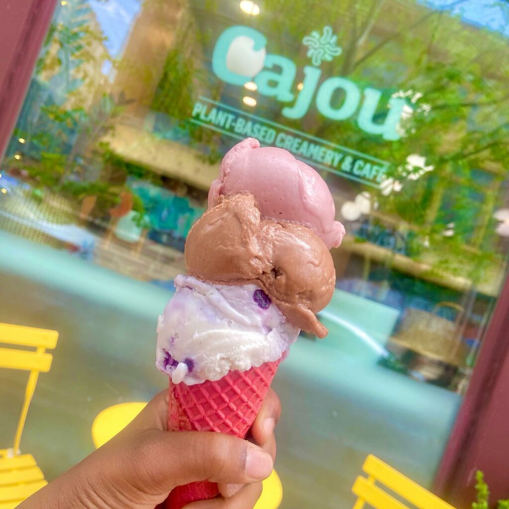 Three scoops of ice cream on a cone in front of cajou creamery